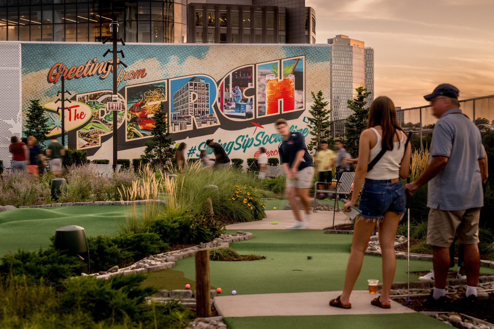 People standing in front of a mural welcoming them to the Perch where they are enjoying a game of mini golf