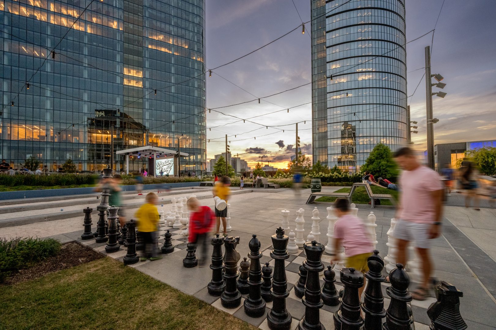Children and adults enjoy a game of giant chess in the neighborhood plaza surrounding Heming apartments